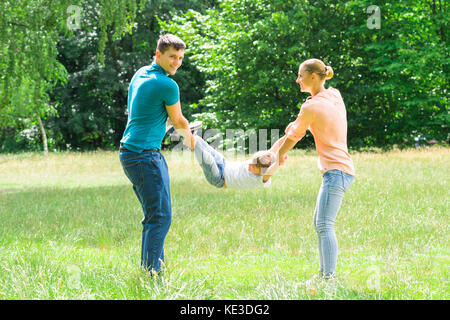 Smiling Young Parent balançant leur fils dans le parc Banque D'Images