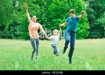 Heureux heureux parents se tenant mains sautant avec leur fils dans le parc Banque D'Images