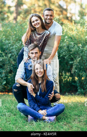 Les hommes et les femmes sur la nature. Quatre happy friends smiling and looking at camera. Les jeunes filles et garçons assis et debout sur l'herbe. portrait of cheerful pe Banque D'Images