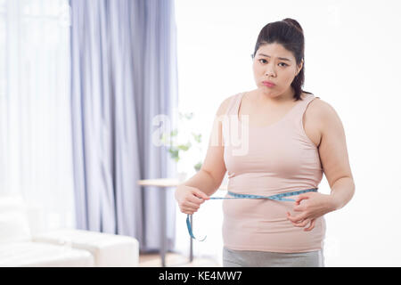 Jeune femme enrobée inquiets measuring her waist Banque D'Images