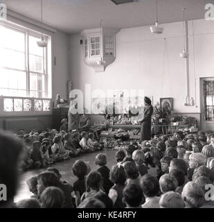 Années 1960, historiques, de l'action de récolte à une école primaire chrétienne, England, UK, les enfants s'asseoir tranquillement à l'Assemblée générale comme l'enseignant explique la récolte et où la nourriture qu'ils consomment provient de. Banque D'Images