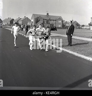 1964, historique, groupe d'adolescents portant des gilets et des tee-shirts et des pilmsollls simples de l'époque sur leurs pieds, en compétition dans une course sur la route, Angleterre, Royaume-Uni. Banque D'Images