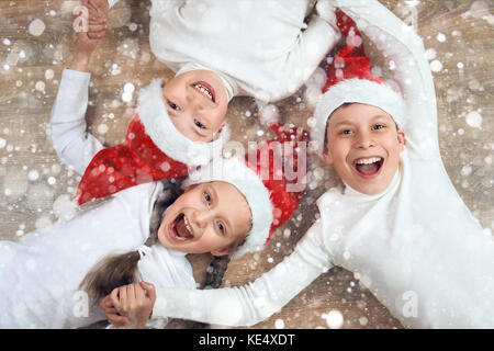 Tenir la main de l'enfant heureux et couché sur fond de bois, vêtu de noël santa hat et le plaisir des vacances d'hiver, neige, concept decoration Banque D'Images