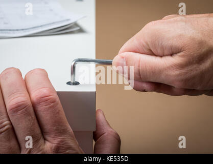 Un homme télévision bâtiment Mobilier pack en utilisant une clé allen avec les instructions de construction dans l'arrière-plan Banque D'Images