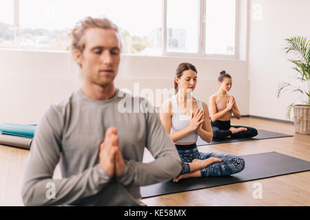 Woman practicing yoga in gym class avec des gens assis autour. Dans lotus poser méditer en étant assis dans la chambre. Banque D'Images