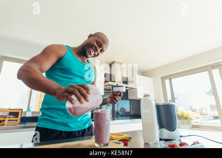 L'homme préparer milk shake en cuisine. Smiling man pouring milk-shake dans un verre pour boire. Banque D'Images