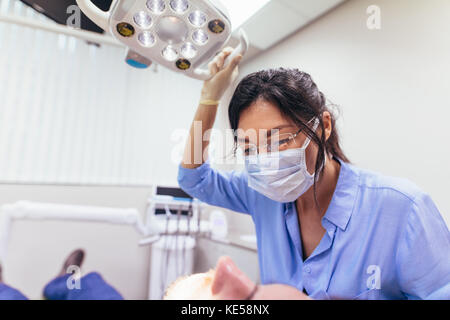 Femme dentiste wearing mask réglage de lumière avec patient sur fauteuil à une clinique dentaire. Femme médecin se préparer à un traitement dentaire sur patient de sexe masculin. Banque D'Images