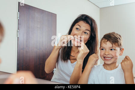 Petit garçon avec sa mère dans la salle de bains nettoyer les dents avec du fil dentaire. Femme avec des fils à la recherche de miroir et nettoyer les dents. Banque D'Images