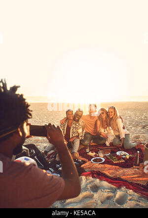 Jeune homme avec un téléphone photo qui photographie des amis en pique-nique plage d'été ensoleillée Banque D'Images