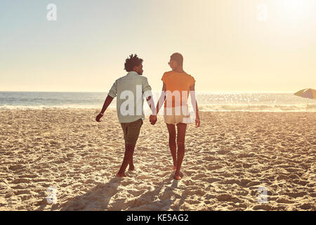 Jeune couple tenant les mains, marchant sur la plage ensoleillée d'été Banque D'Images