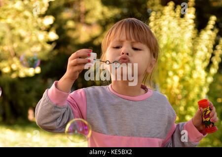 Little girl blowing bubbles avec green scenery derrière Banque D'Images