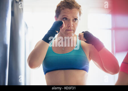 Déterminé boxer féminin avec enveloppements de poignet en position de combat à salle de sport Banque D'Images