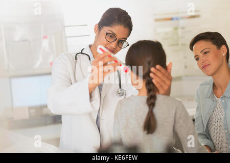 Femme médecin utilisant un thermomètre numérique dans l'oreille d'une jeune patiente dans la salle d'examen Banque D'Images