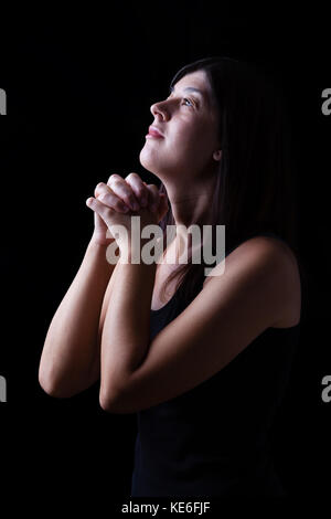 Femme en prière dans l'adoration fidèle à Dieu jusqu'à la dans l'espoir, avec les mains croisées et de ferveur religieuse sur un fond noir. foi prière sourire souriant Banque D'Images