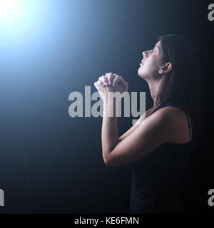 Femme en prière dans l'adoration fidèle à Dieu jusqu'à l'espoir, dans le cadre d'une lumière céleste ou divine prière prière spiritualité foi. iluminated céleste Banque D'Images