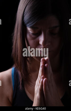 Fidèles priant femme athlétique, les mains croisées dans le culte à Dieu, la tête en bas et les yeux fermés dans l'inspiration religieuse. fond noir. la prière prier portrait Banque D'Images