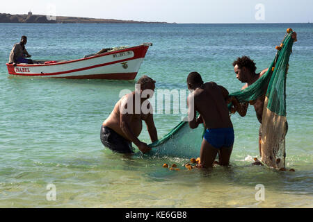 Les pêcheurs préparer un filet dans l'eau jusqu'aux genoux sur une plage avec leur bateau de pêche dans l'arrière-plan Banque D'Images