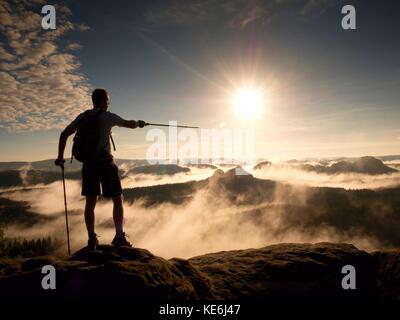 Randonneur avec sac à dos sportif sur rocky view point au-dessus de la vallée brumeuse. sunny daybreak en montagnes rocheuses après nuit pluvieuse. Banque D'Images