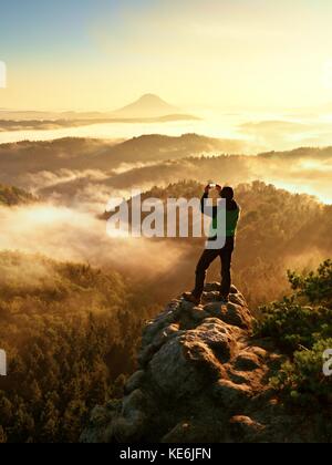 Silhouette homme haut escalade sur falaise. randonneur est montée jusqu'au pic de profiter de la vue. l'homme veille sur misty et matin brumeux en vallée de soleil du matin. Banque D'Images