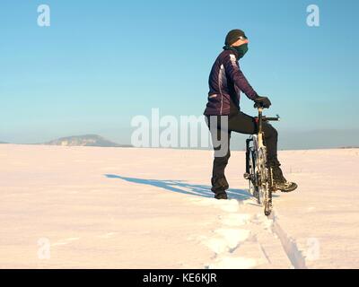 Biker poussant VTT sur neige gel. d'hiver ensoleillée. météo biker vélo pousse dans la neige profonde en prairie. incroyable journée ensoleillée. petit snow fl Banque D'Images