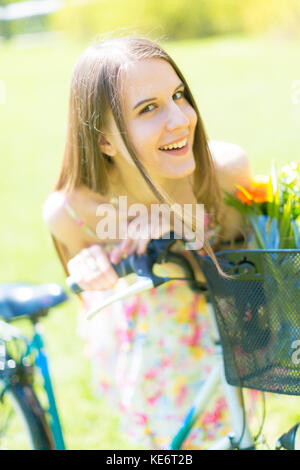 Portrait de jeune belle femme aux cheveux longs en été Parc. à côté d'un vélo avec un panier de fleurs Banque D'Images