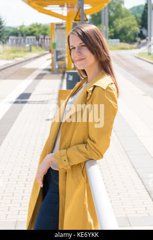 Jeune femme dans un ciré en attente d'un train en gare Banque D'Images