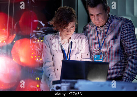 Techniciens INFORMATIQUES travaillant sur un ordinateur portable dans une salle de serveurs sombre Banque D'Images
