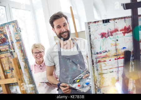 Portraits souriants artistes peignant sur des chevalets dans un studio de classe artistique Banque D'Images