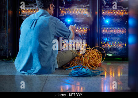 Technicien informatique mâle avec câbles sur le panneau du serveur sombre chambre Banque D'Images