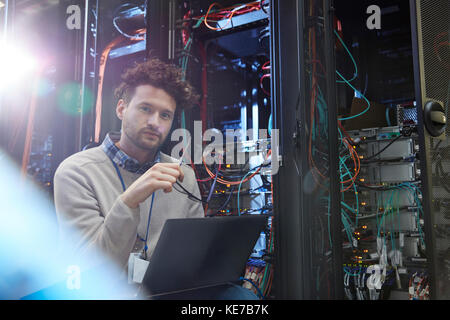 Portrait homme confiant TECHNICIEN INFORMATIQUE travaillant à un ordinateur portable dans un serveur chambre Banque D'Images