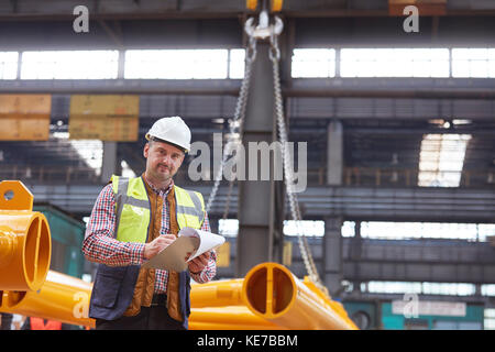 Portrait contremaître homme confiant écrivant sur presse-papiers en usine Banque D'Images