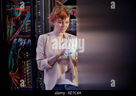 Femme TECHNICIENNE INFORMATIQUE utilisant une tablette numérique futuriste dans la salle des serveurs Banque D'Images