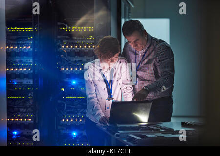 Techniciens INFORMATIQUES travaillant sur un ordinateur portable dans une salle de serveurs sombre Banque D'Images