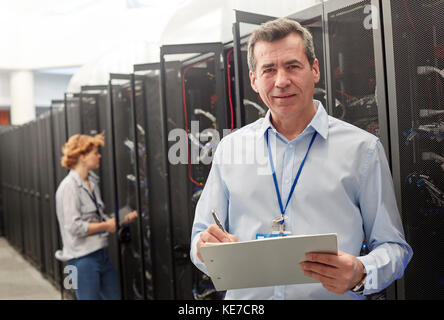 Portrait homme confiant TECHNICIEN INFORMATIQUE avec presse-papiers dans la salle des serveurs Banque D'Images