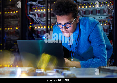 Technicien INFORMATIQUE spécialisé travaillant sur un ordinateur portable dans un serveur sombre chambre Banque D'Images