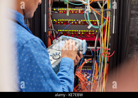 Technicien INFORMATIQUE utilisant un équipement de test de fibre optique dans la salle des serveurs Banque D'Images