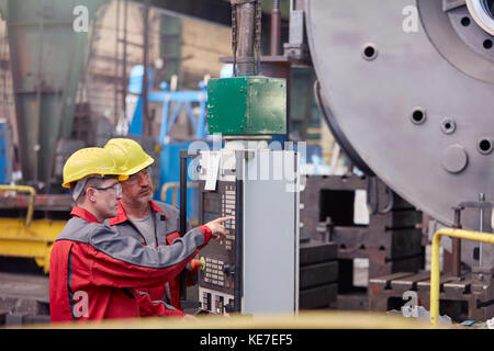 Les hommes qui utilisent des machines au tableau de commande en usine Banque D'Images