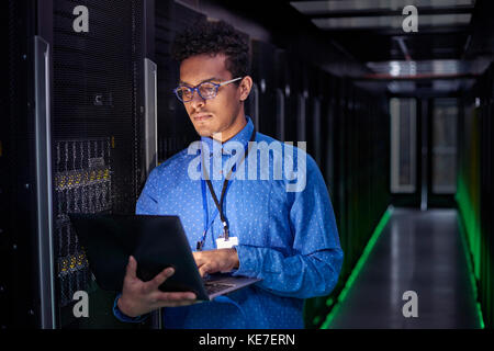 Un technicien INFORMATIQUE spécialisé utilisant un ordinateur portable dans une salle de serveurs sombre Banque D'Images