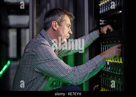 Un technicien INFORMATIQUE spécialisé travaillant sur un panneau dans un serveur sombre chambre Banque D'Images