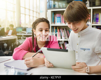 Souriant étudiant à la recherche, en utilisant une tablette numérique à table dans la bibliothèque Banque D'Images