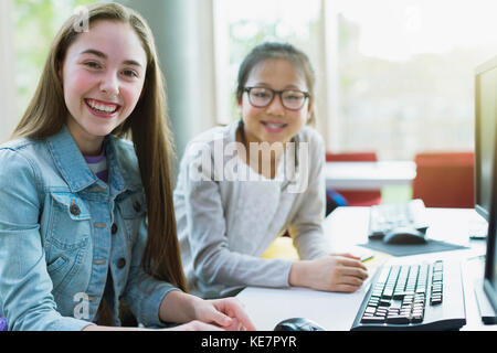 Portrait souriant, confiante jeune fille étudiant à la recherche à l'ordinateur dans la bibliothèque Banque D'Images