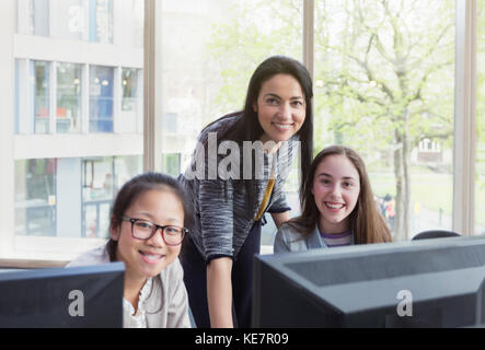 Portrait confiante, souriante enseignante et des jeunes filles recherchant à l'ordinateur dans la bibliothèque Banque D'Images