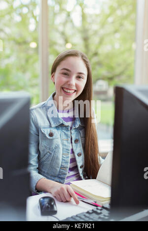 Portrait souriant, confiante jeune étudiante à la recherche à l'ordinateur dans la bibliothèque Banque D'Images