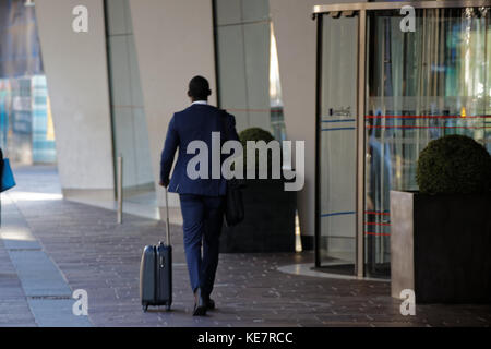 Homme noir dans un costume bleu avec sac valise trolley entrant sortant de l'entrée de la porte tournante de l'hôtel Radisson Blu Hotel, Glasgow Banque D'Images