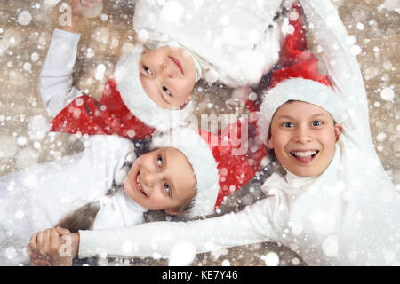 Tenir la main de l'enfant heureux et couché sur fond de bois, vêtu de noël santa hat et le plaisir des vacances d'hiver, neige, concept decoration Banque D'Images