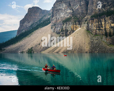 Un canoë rouge dans le lac Moraine avec une falaise des Rocheuses canadiennes le long du rivage ; Lake Louise, Alberta, Canada Banque D'Images