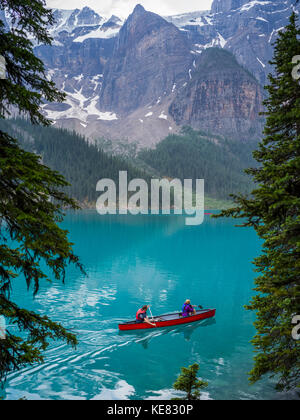 Un canoë rouge dans le lac Moraine avec une falaise des Rocheuses canadiennes le long du rivage ; Lake Louise, Alberta, Canada Banque D'Images