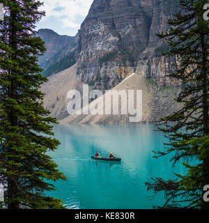 Un canoë rouge dans le lac Moraine avec une falaise des Rocheuses canadiennes le long du rivage ; Lake Louise, Alberta, Canada Banque D'Images