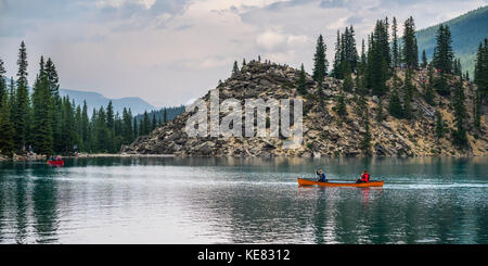 Un canoë rouge dans le lac Moraine avec une falaise des Rocheuses canadiennes le long du rivage ; Lake Louise, Alberta, Canada Banque D'Images