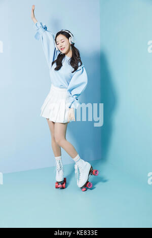 Young smiling woman wearing headphones et patins à posant avec ses yeux fermés Banque D'Images